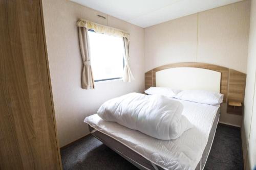 滨海克拉克顿8 Berth Caravan At Highfield Grange In Essex Ref 26267e的一间卧室配有一张带白色床单的床和一扇窗户。