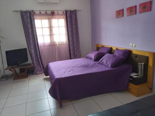 阿比让MC Location的一间卧室配有一张紫色的床和一台电视机