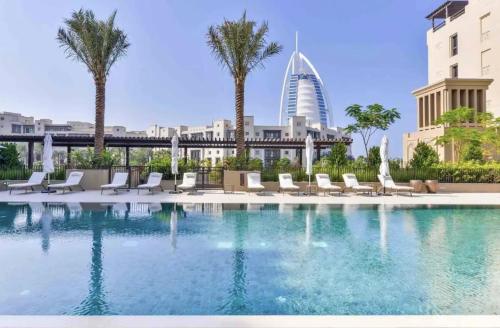 迪拜Madinat Jumeirah Living, MJL Dubai的一座带椅子和棕榈树的游泳池以及一座建筑