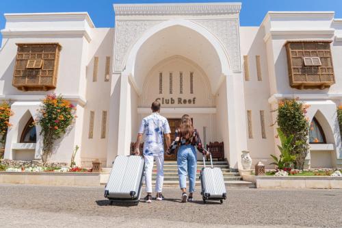 沙姆沙伊赫Club Reef Resort & Spa的男人和女人在大楼前带着行李走路