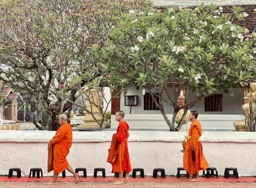 琅勃拉邦Barn Laos Luangprabang Hostel的三名僧侣在一座建筑物前行走