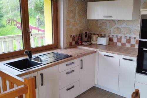 旺特龙Maison de montagne vue magnifique的厨房配有白色橱柜、水槽和窗户。