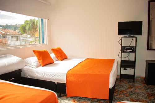 波哥大Hotel BogoSuba 127的客房设有两张带橙色枕头的床和窗户。
