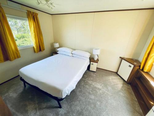 SouthminsterSuperb Caravan At Steeple Bay Holiday Park In Essex, Sleeps 6 Ref 36081d的卧室配有一张白色大床和黄色窗帘