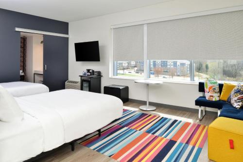 夏洛特Aloft Charlotte Airport的卧室配有白色的床和色彩缤纷的地毯。