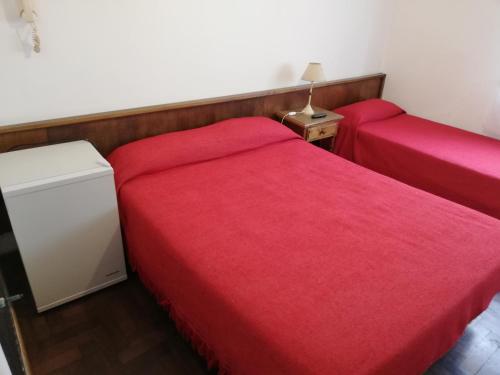 内科切阿Necochea Real Hotel的一间卧室配有两张带红色床单的床和床头柜