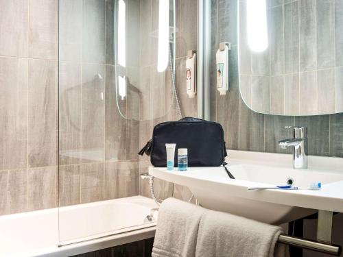 科涅克Hôtel Ibis Cognac Centre的浴室设有水槽和淋浴,浴室内备有袋子