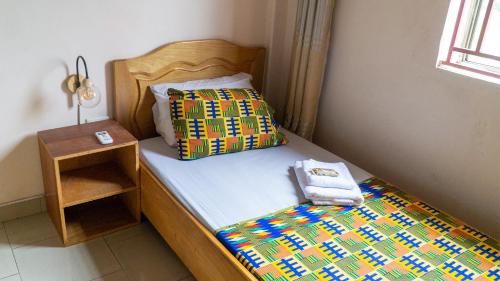 库马西Sign of Silence Hostel的一张带五颜六色的被子和床头柜的床