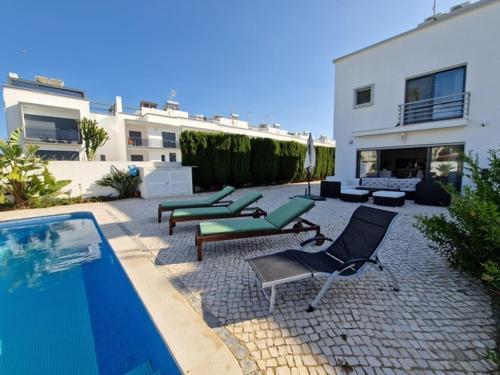 维拉诺瓦德卡塞拉Beachfront house,Manta Rota,Algarve的一个带椅子的庭院和一个毗邻房子的游泳池