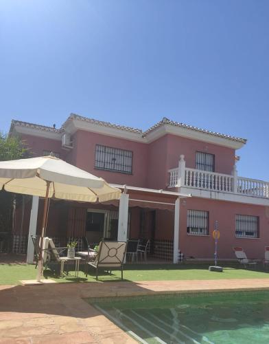 格拉纳达Villa 28 de julio Casa Rural con piscina en Granada的粉红色的房子,配有椅子和遮阳伞,设有一个游泳池