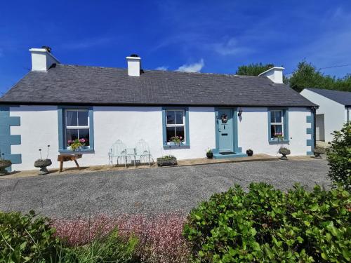 多尼戈尔New Listing - Ladybird Cottage - Donegal - Wild Atlantic Way的白色的房子,设有蓝色的门和椅子