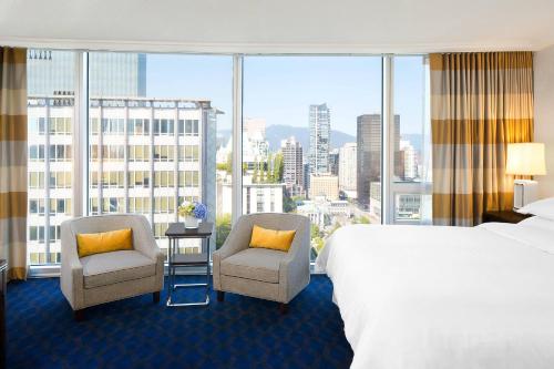 温哥华温哥华喜来登华尔中心酒店的酒店客房设有一张床铺、两把椅子和一个大窗户。