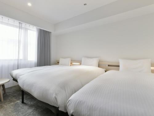 熊本REF Kumamoto by VESSEL HOTELS的配有白色床单的酒店客房内的两张床