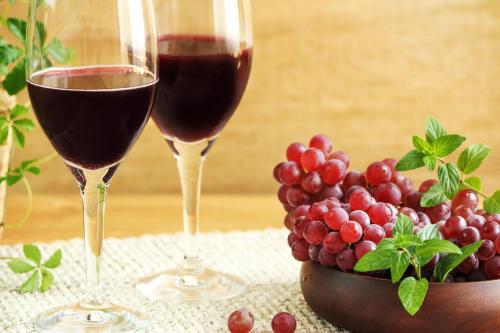 驹根市ホテル南の風風力3駒ヶ根店的两杯红葡萄酒,紧挨着一碗葡萄