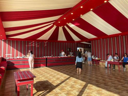 亚喀巴Wadi Rum Gulf camp的舞厅,有红色和白色的帐篷,有吃的人