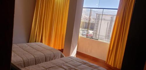 库斯科A un minuto del aeropuerto Siéntase como en casa的客房设有两张床和一个带黄色窗帘的窗户。