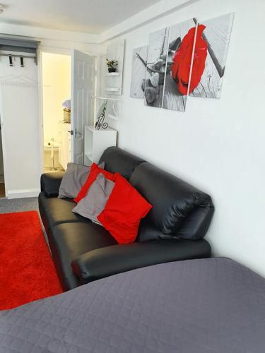米尔顿凯恩斯Richfieldsat59的客房内的黑色皮革沙发,配有红色枕头