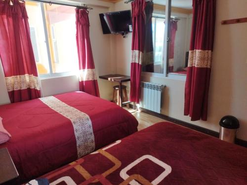 乌尤尼Uyuni HOSTAL YOKOSO的配有两张床铺、红色窗帘和电视的客房