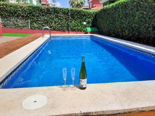 佩尼斯科拉URBANIZACION MIRAMAR PENISCOLA的游泳池旁的一瓶葡萄酒和两杯酒