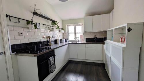 史云顿Converted Railway Cottage的厨房配有白色橱柜和黑炉灶烤箱。