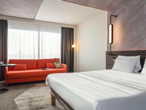 鹿特丹鹿特丹布莱恩诺富特酒店的酒店客房,配有一张床和一张红色的沙发