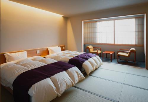 云仙市云仙新汤温泉日式旅馆的配有窗户和椅子的客房内的两张床