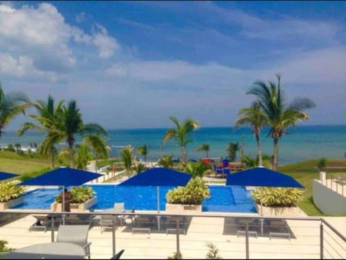 圣卡洛斯Lujoso y Familiar Apartamento de Playa y Golf en San Carlos Panamá的一个带蓝伞和海洋的游泳池