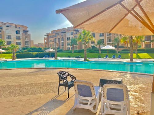 开罗Ultra Luxury 3BR with Pools ,Sports ,Dining in Gated compound, Close to all sites的游泳池旁的两把椅子和一把遮阳伞