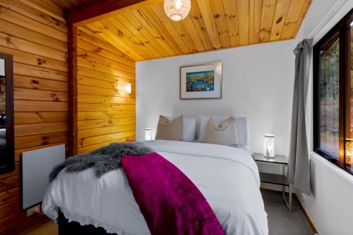 皇后镇Kereru Cottage, Romantic & Beautiful Log Cabin - Queenstown的卧室配有白色床和紫色毯子