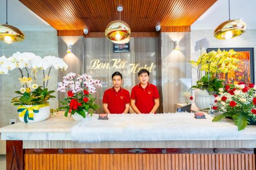 胡志明市Bonka Hotel Luxury Quận 5 HCM的两个男人站在柜台后面,花朵