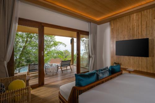 普吉镇Sinae Phuket - SHA Extra Plus的一间卧室设有一张床、一台电视和一个阳台。