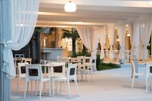 乐托卡亚Olympian Bay Grand Resort的一间设有白色椅子和桌子及窗帘的餐厅