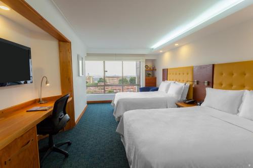 麦德林Four Points by Sheraton Medellín的酒店客房设有两张床、一张桌子和一台电视。