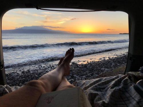 基黑Campervan/Maui hosted by Go Camp Maui的一个人躺在海滩上,脚踏着书