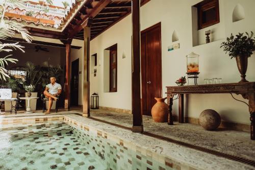 卡塔赫纳圣托里维奥精品酒店的坐在带游泳池的房子旁椅子上的女人