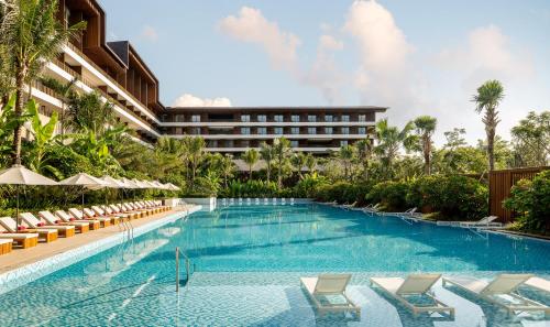 三亚三亚泰康之家度假酒店·臻品之选 (万豪旗下原木设计酒店)的一个带椅子的游泳池和一个位于酒店后面的酒店