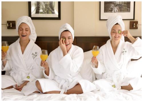 帕兰加Kerpė Hotel & SPA的三个女人坐在床上,喝杯酒