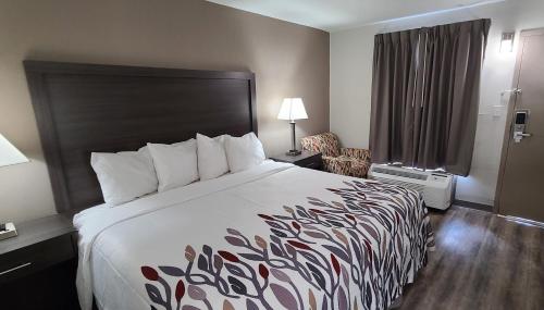 邓肯Red Roof Inn & Suites Duncan的酒店客房带一张大床和一把椅子