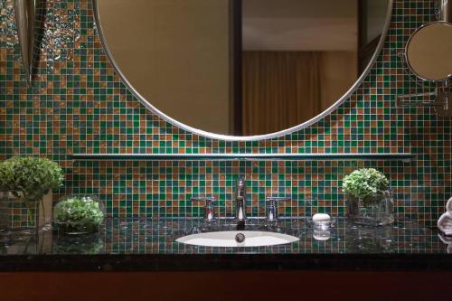 武汉武汉光明万丽酒店的浴室水槽、绿色瓷砖墙和镜子