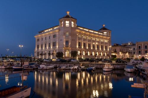 锡拉库扎Ortea Palace Hotel, Sicily, Autograph Collection的码头上的一个大型建筑,晚上有船只
