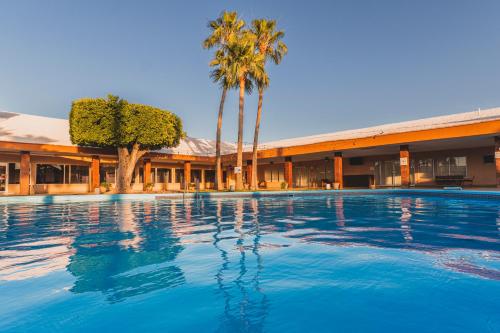 Heroica CaborcaEl Camino Hotel & Suites的棕榈树建筑前的游泳池
