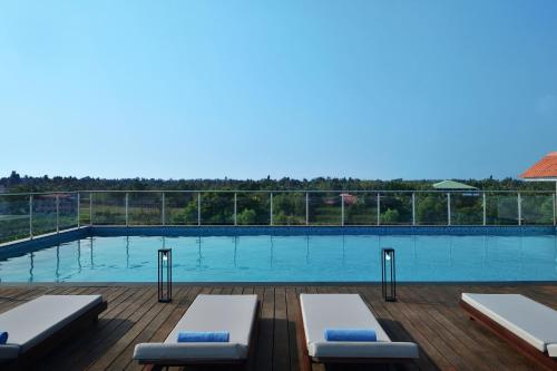 尼杜巴塞莱Port Muziris, A Tribute Portfolio Hotel的木制甲板上的游泳池,配有2张躺椅