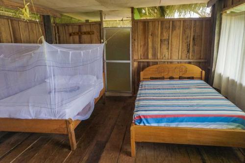 YucurucheLibertad Jungle Lodge的一间带两张床铺的卧室,位于带木墙的房间内