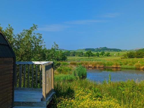 KeltyPond View Pod 2 with Private Hot Tub -Pet Friendly- Fife - Loch Leven - Lomond Hills的田野旁的一条河上的木桥