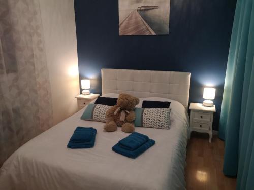 TonneinsLa Roseraie的泰迪熊坐在床上,床上摆着蓝色枕头