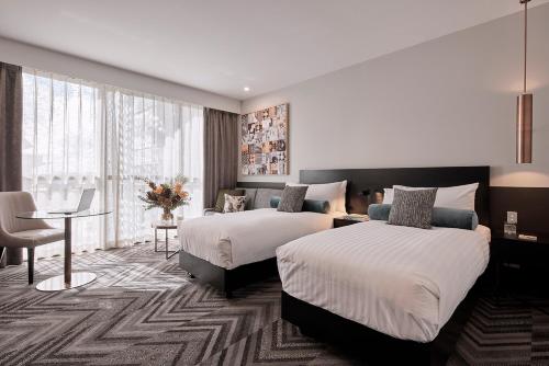 珀斯Rydges Perth Kings Square的酒店客房设有两张床、一张桌子和一张桌子。