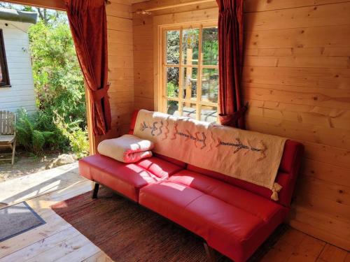 康威Tan y coed's Rosemary Cabin的红色沙发,坐在带窗户的房间