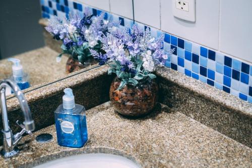 圣保罗Flat BOUTIQUE em frente ao metrô MOEMA的浴室水槽,内有一瓶肥皂和紫色鲜花
