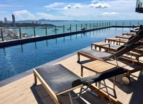 芭堤雅市中心BASE Central PATTAYA Long Balcony with Infinity Pool & Free Netflix!的游泳池顶上的一排躺椅