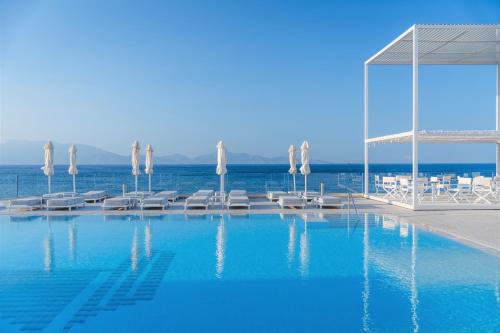 Ágios FokásDimitra Beach Hotel & Suites的一个带遮阳伞和椅子的游泳池以及大海